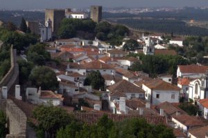 Blick von der Stadtmauer auf rote Dächer, weiße Häuser und Burg von Óbidos.