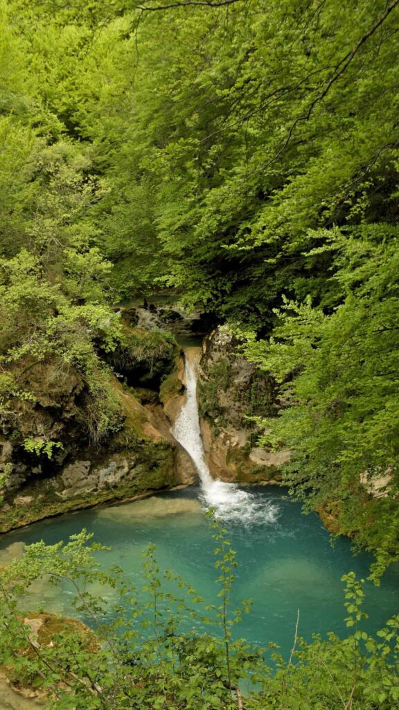 Kleiner Wasserfall mit türkisblauem Becken in einem üppig grünen Wald im Norden Navarras.