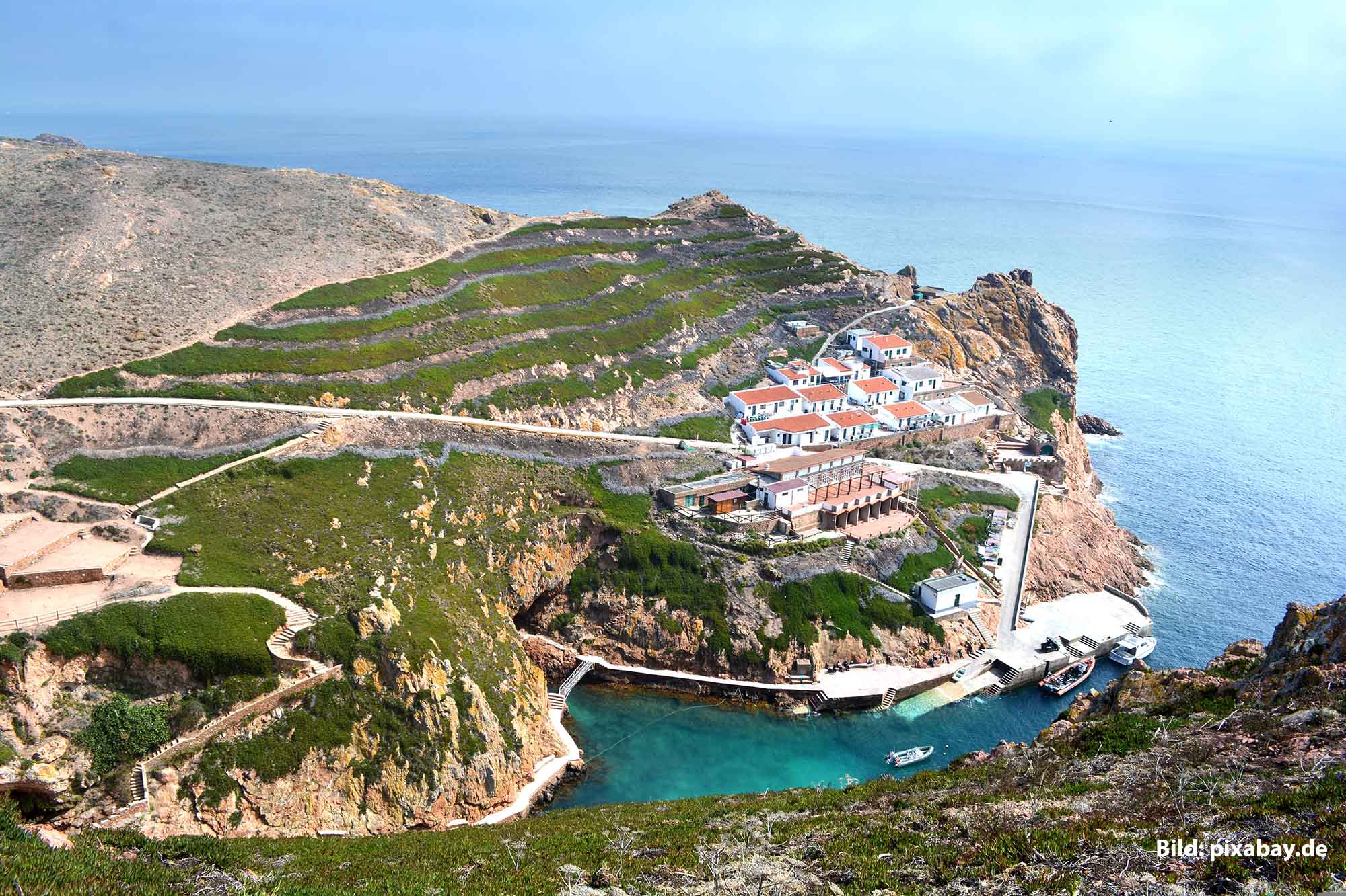 Vogelperspektive auf die Insel Berlenga Grande mit Terrassenlandschaft, weiß-roten Gebäuden und dem türkisfarbenen Atlantik vor der Küste Portugals.