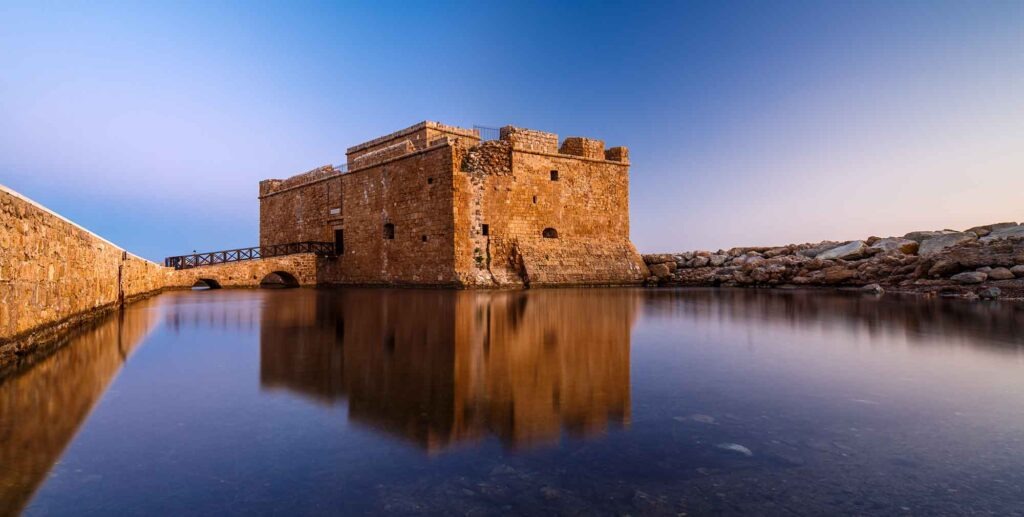 Steinernes Kastell von Pafos mit einer Zugangsbrücke und Spiegelung im stillen Hafenwasser.