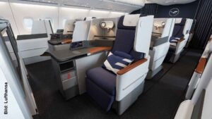 Blick in die Lufthansa Business Class des Airbus A380 mit versetzt angeordneten Einzelsitzen, breiten Armlehnen in Holzoptik, großer Ablagefläche, Leselampen und blau gepolsterten Sitzen.