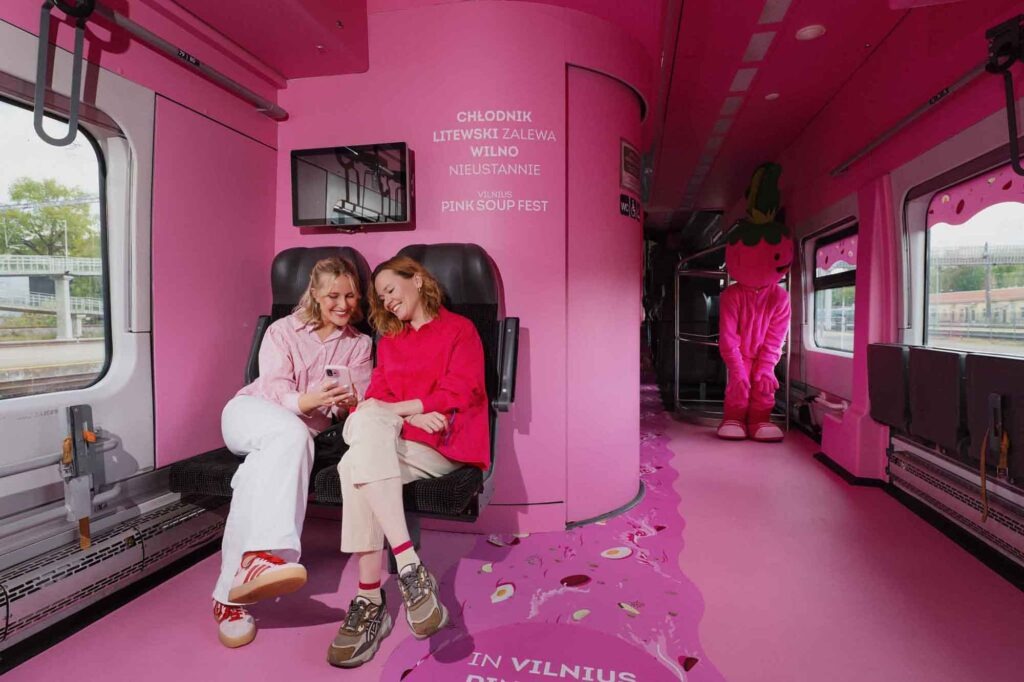 Pink dekoriertes Zugabteil mit Besucherinnen und Maskottchen des Vilnius Pink Soup Fest 2026.