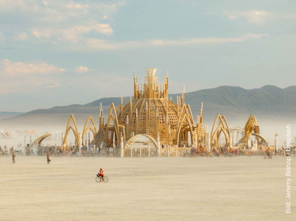 Monumentale tempelartige Holzinstallation beim Burning Man in der Black Rock Desert, im Vordergrund fährt ein Radfahrer über die Playa.