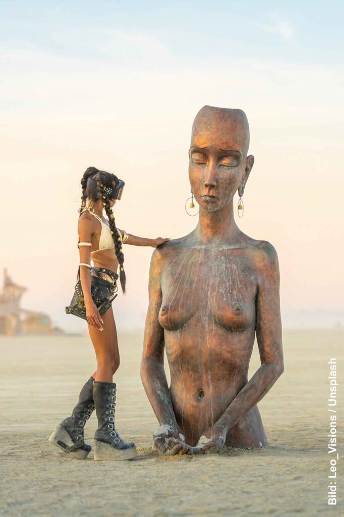 Besucherin neben einer großen weiblichen Skulptur auf der Playa beim Burning Man in der Wüste von Nevada.