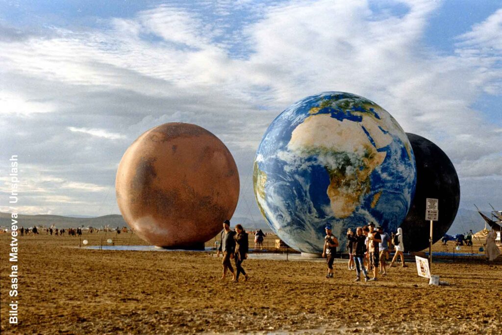 Große kugelförmige Kunstinstallationen beim Burning Man, darunter eine als Erde gestaltete Kugel, mit Besuchern auf der Playa.