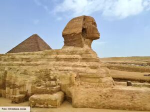 Die Große Sphinx von Gizeh, im Hintergrund eine Pyramide