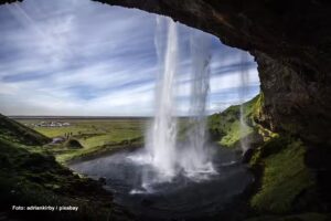 Blick aus einer Höhle durch den Wasserfall hindurch auf die umgebende Landschaft