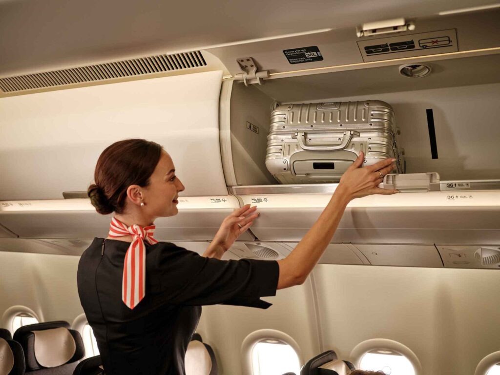 Condor: Flugzeuge, Kabinen und Service 26 Flugbegleiterin legt einen Alukoffer in die Gepäckablage