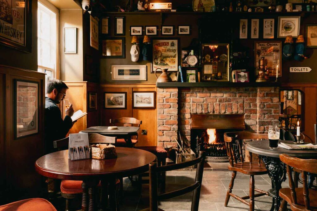 Whiskeyhotel-Innenaufnahme der stimmungsvollen Whiskey-Bar mit offenem Kamin, Holztischen und zahlreichen Vintage-Dekorationen