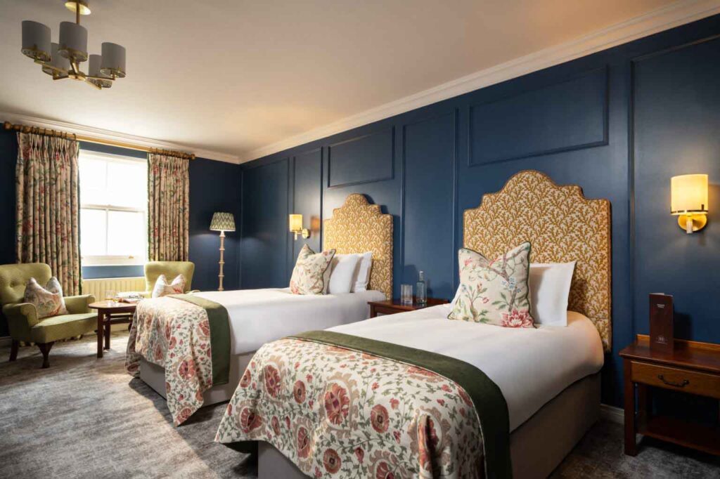 Doppelzimmer mit zwei Betten, stilvoll dekoriert in Blau, Gold und floralen Stoffen, mit klassischer Möblierung