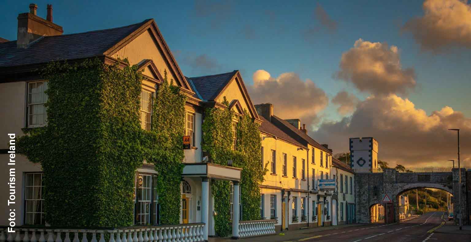 Mit Efeu bewachsene Fassade des Harbourview Hotels in Carnlough, daneben die historische Straßenbrücke im warmen Abendlicht