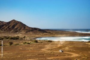 Inselhopping auf den Kapverden: Zwischen Vulkaninseln, Tropengrün und kolonialem Flair 18 Blick auf Wüstenland mit Bergen und Bucht und einige 4WD-Fahrzeugen
