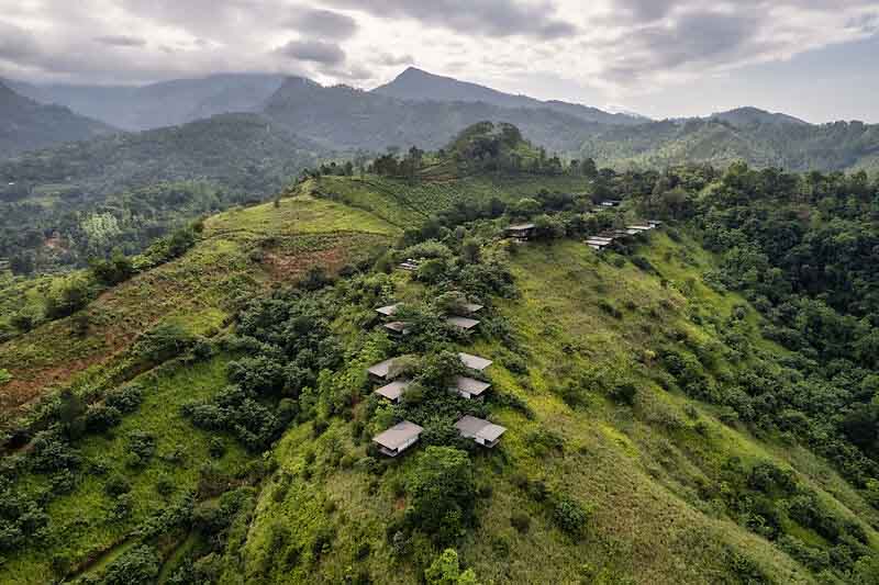 Santani Wellness Kandy: Luxus, Achtsamkeit und Natur im Einklang 4 Luftaufnahme der Chalets im Santani Wellness Resort auf grünem Berghang mit üppigem Dschungel und Bergen im Hintergrund.