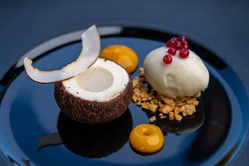 Santani Wellness Kandy: Luxus, Achtsamkeit und Natur im Einklang 7 Feines Dessert mit Kokos, Eis und Fruchtkomponenten auf schwarzem Teller im Santani Wellness Resort.