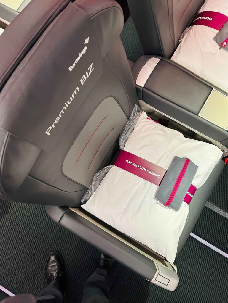 Detail des neuen Eurowings Premium BIZ Sitzes mit Kopfstütze, großem Kissen und Amenity Kit auf der Sitzfläche, aus der Kabinenperspektive von oben fotografiert.