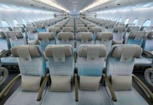 Emirates A380 Sitzplätze und Services - die Fotos 15 Blick durch die lange Kabine der Economy Class eines Großraumflugzeugs. Die Sitze sind in einer 3-4-3-Anordnung aufgeteilt und mit hellen Stoffbezügen in Weiß, Blau und dezenten Mustern sowie grauen Lederkopfstützen ausgestattet.