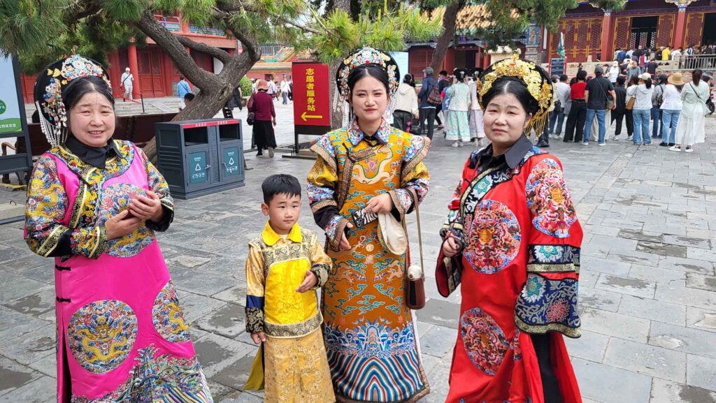 Kaiserpalast von Shenyang – Die „Verbotene Stadt“ des Nordens erleben 3 Kaiserpalast von Shenyang. Vier Personen – darunter ein Kind – in bunten, traditionellen Qing-Gewändern stehen lächelnd im Hof des Shenyang-Kaiserpalasts; historische Gebäude im Hintergrund.