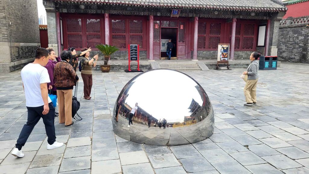 Kaiserpalast von Shenyang – Die „Verbotene Stadt“ des Nordens erleben 13 Große spiegelnde Halbkugel im Hof des Shenyang-Palasts; Reflexion von Besuchern und Gebäuden sichtbar.