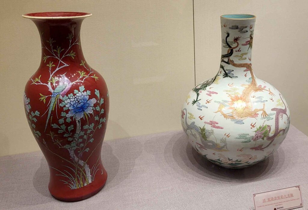 Kaiserpalast von Shenyang – Die „Verbotene Stadt“ des Nordens erleben 15 Zwei antike chinesische Porzellanvasen stehen auf einem Podest. Die linke Vase ist leuchtend rot mit einem blauen Blumendesign. Die rechte Vase ist weiß mit bunten Drachen- und Vogelmotiven.