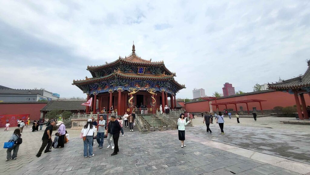 Kaiserpalast von Shenyang – Die „Verbotene Stadt“ des Nordens erleben 10 Eine Weitwinkelansicht des Chongzheng-Palastes, einem großen, mehrstöckigen Gebäude mit einem reich verzierten Dach, roten Säulen und farbenfrohen Holzarbeiten, umgeben von einem großen gepflasterten Platz.