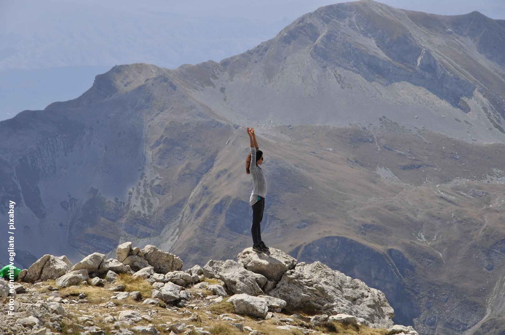 Frau vor Bergmassiv streckt die Arme in die Höhe