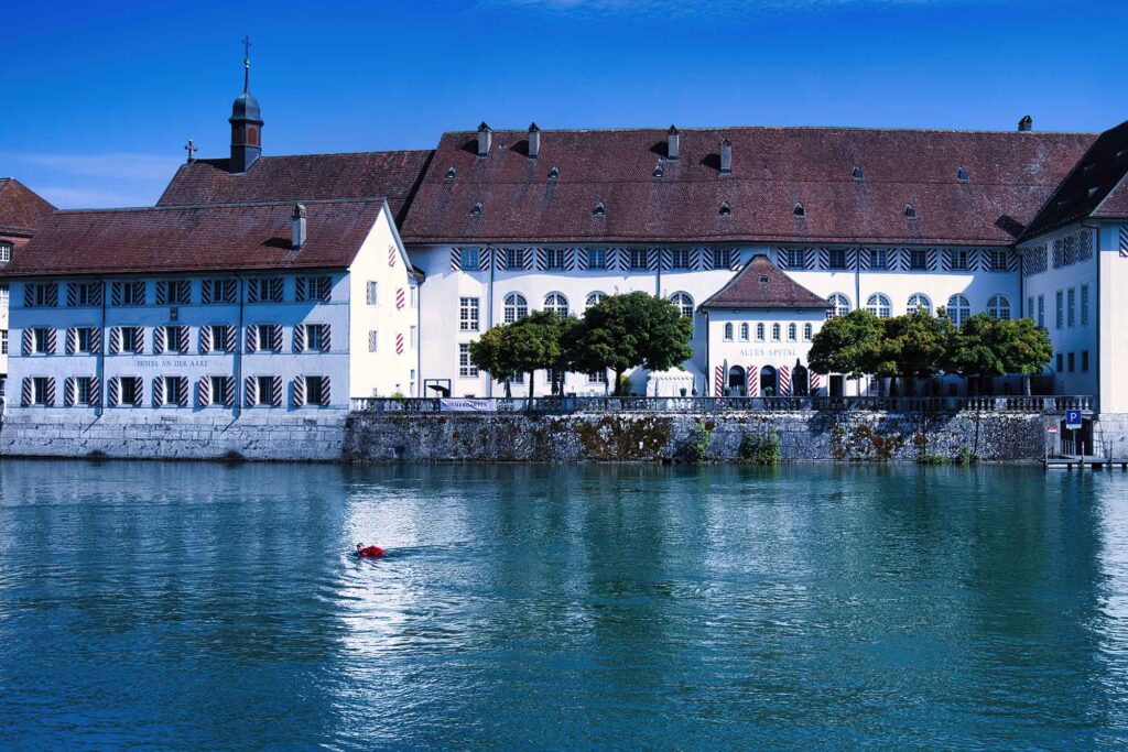 Durch eiskaltes Wasser und Stromschnellen schwimmen 6 Schwimmer in der Aare vor barocker Architektur in Solothurn, Schweiz