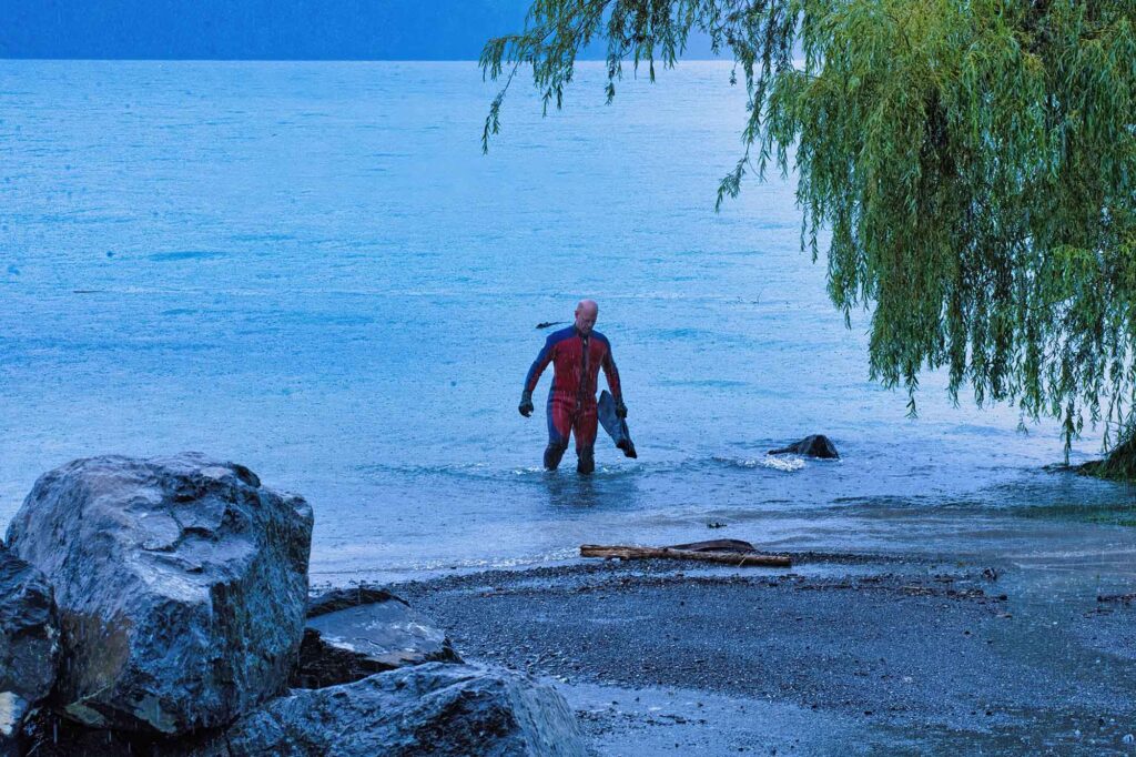 Durch eiskaltes Wasser und Stromschnellen schwimmen 7 Schwimmer steigt im Regen aus dem Brienzersee, graue Stimmung mit Seeufer und Bäumen