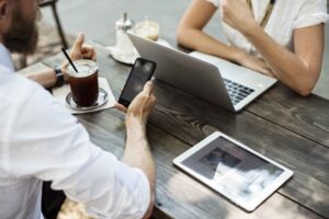 Zwei Personen sitzen am Tisch mit Laptop, Tablet und Handy