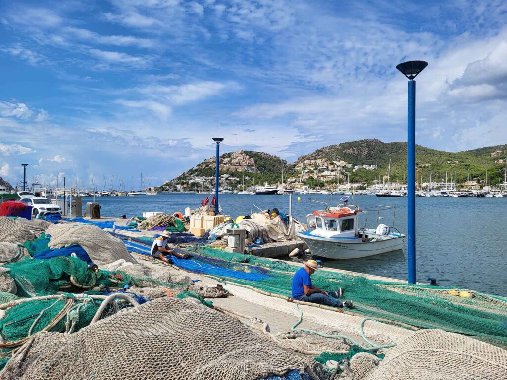 Fischer in Puerto de Andratx reparieren Netze am Hafen mit Blick auf Bucht und Yachten.