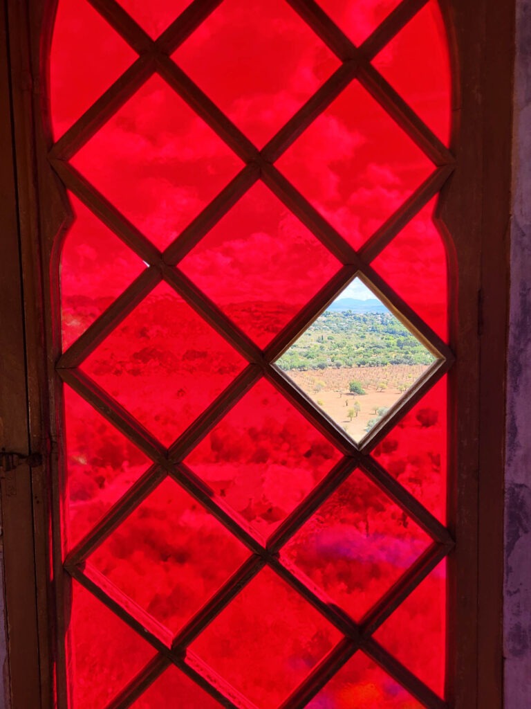 lick durch ein rotes Buntglasfenster im Landgut Raixa auf Mallorca mit Ausblick auf die umliegende Landschaft.