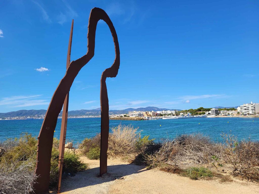 Palma de Mallorca – Sehenswürdigkeiten zwischen Geschichte und Meer 9 Das Foto zeigt eine moderne, abstrakte Skulptur aus rostigem Stahl, die an der Küste direkt am Meer steht.
