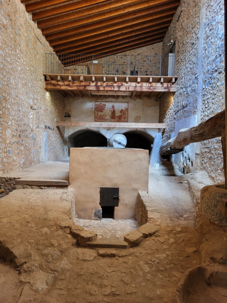 Innenansicht der alten Ölmühle im Landgut Raixa auf Mallorca mit Steinmauern, Balkendecke und Mahlwerk.