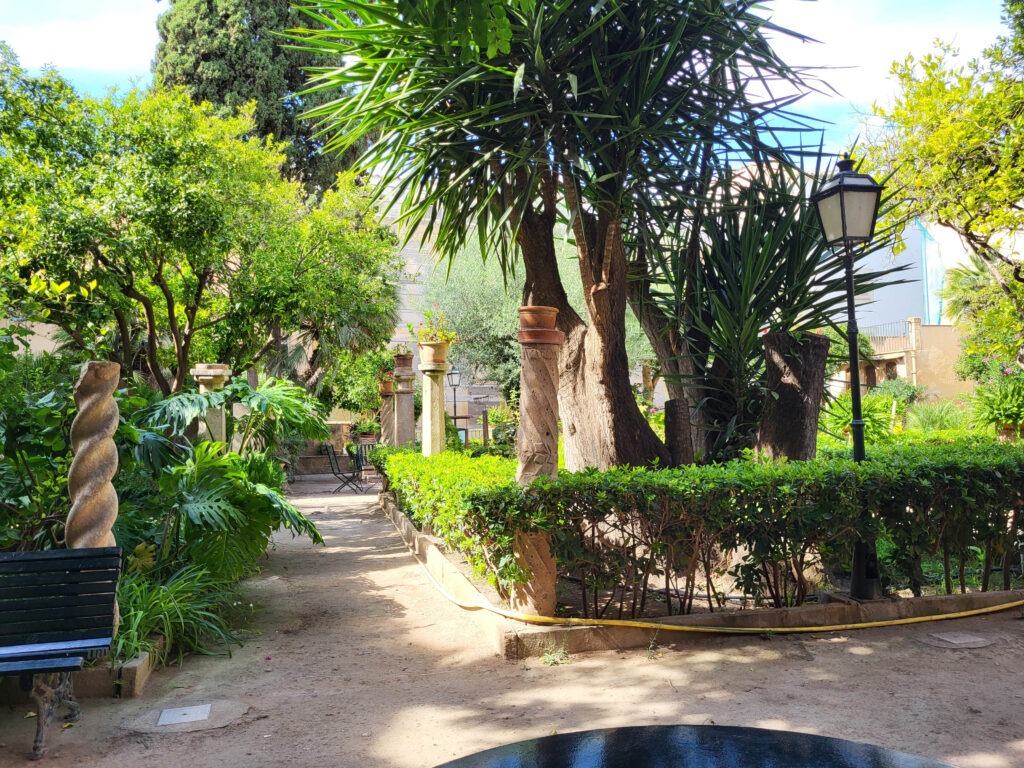 Palma de Mallorca – Sehenswürdigkeiten zwischen Geschichte und Meer 11 Historischer Garten in Palma mit üppiger Vegetation, Steinornamenten, Bänken und mediterranen Pflanzen.