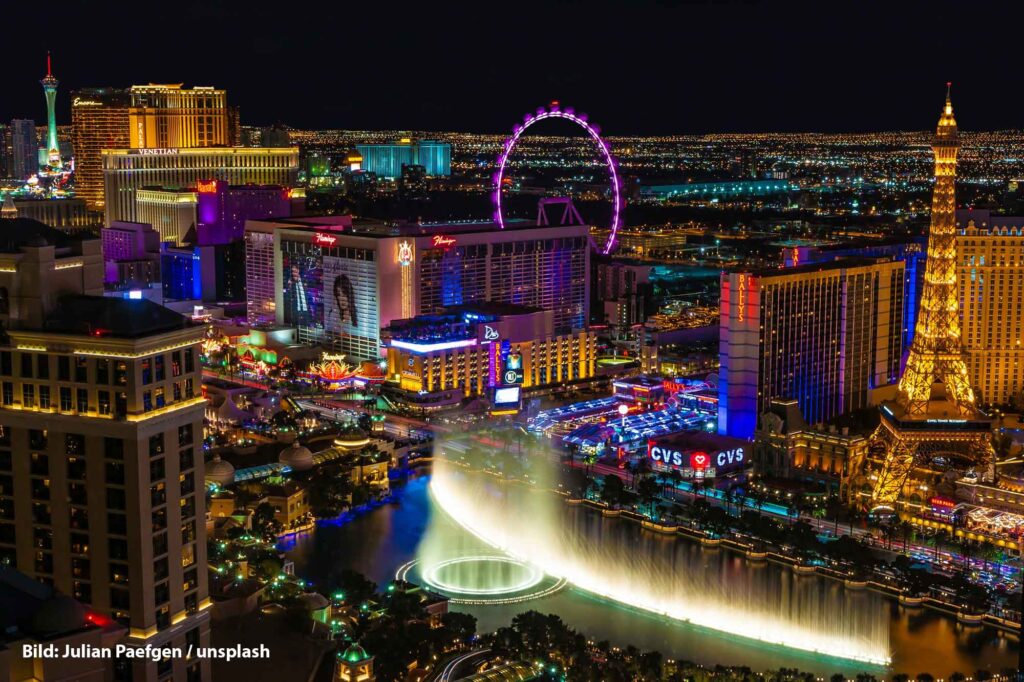 Panorama des Las Vegas Strip bei Nacht mit hell erleuchteten Casinos, dem Bellagio-Brunnen im Vordergrund und zahlreichen Wahrzeichen wie dem nachgebauten Eiffelturm.
