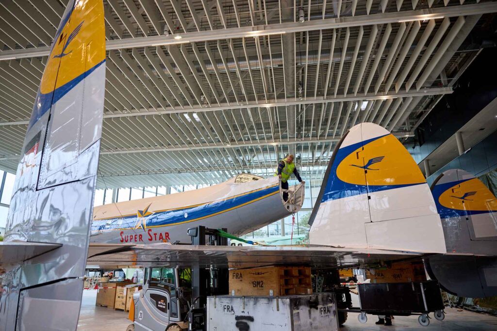 Zwei Lufthansa-Legenden vereint: Ju 52 und Lockheed Super Star in einer Ausstellung 6 Ein Techniker montiert am Leitwerk der restaurierten Lufthansa Lockheed Super Star im Hangar One, während die markant lackierten Heckflossen im Vordergrund zu sehen sind.