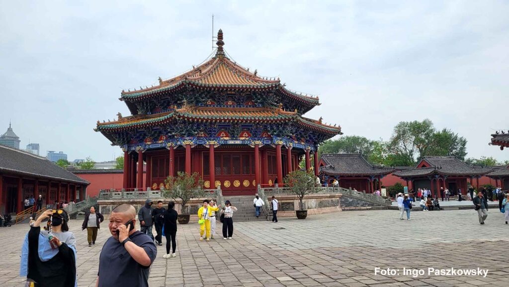 Kaiserpalast Shenyang – Die „Verbotene Stadt“ des Nordens erleben 20 Eine Weitwinkelansicht des Chongzheng-Palastes, einem großen, mehrstöckigen Gebäude mit einem reich verzierten Dach, roten Säulen und farbenfrohen Holzarbeiten, umgeben von einem großen gepflasterten Platz.
