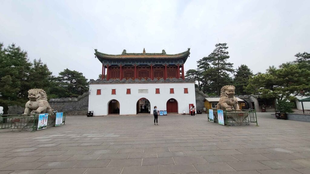 Weißes Gebäude mit drei Torbögen und einem gelb-goldenen Ziegeldach, bewacht von zwei großen Steinlöwen.