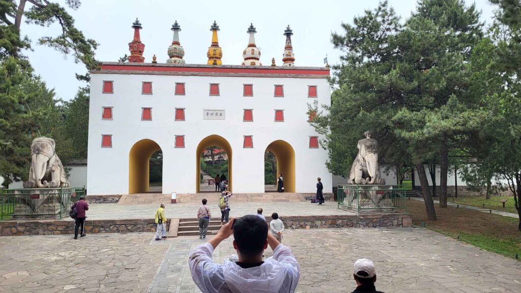 Ein weißes Torbauwerk mit drei Durchgängen, auf dessen flachem Dach fünf bunte, kleine Pagoden stehen.