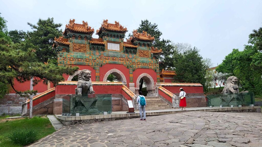 Ein dreibogiges Tor, reich verziert mit grün-gelben Glasurfliesen und Drachenmotiven auf einer roten Basis.