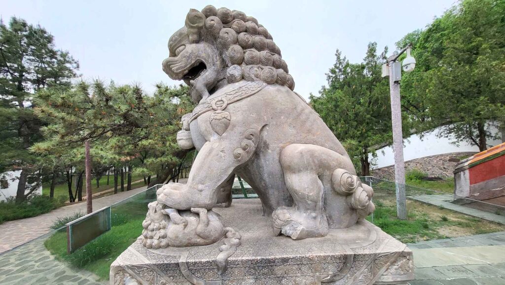 Nahaufnahme einer Steinlöwin, deren Tatze schützend auf einem kleinen Löwenjungen ruht; filigrane Steinmetzarbeit.