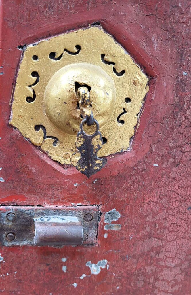 Nahaufnahme eines rostigen Eisenriegels und eines herzförmigen goldenen Beschlags auf verwittertem rotem Holz.