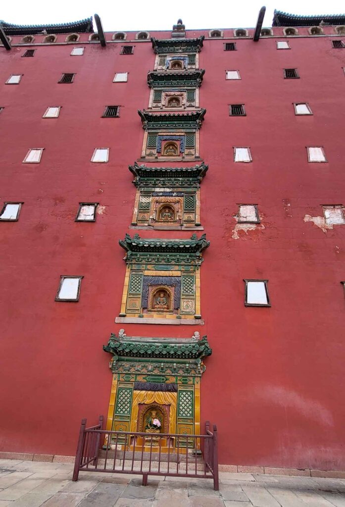 Detailansicht der roten Tempelwand mit mehreren Buddha-Nischen im Putuo Zongcheng Tempel