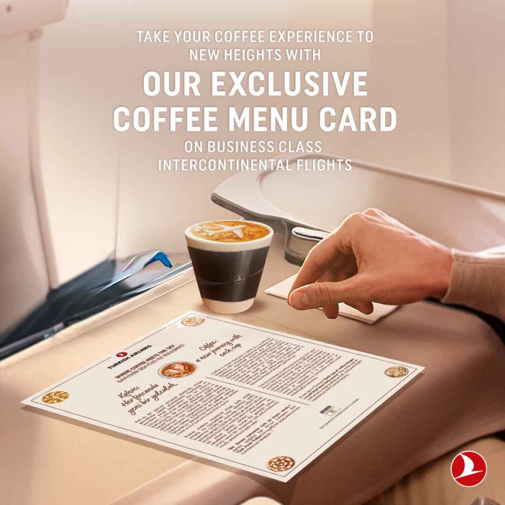 Eine Kaffee-Reise mit Turkish Airlines - Schluck für Schluck um die Welt 3 Business-Class-Tisch im Flugzeug mit Becher Kaffee und ausliegender Kaffee-Menükarte, daneben die Hand eines Passagiers auf dem aufgeklappten Tabletttisch.
