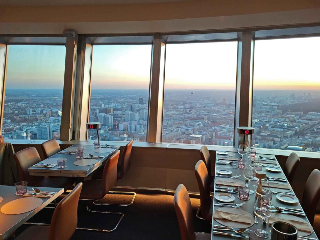 Innenraum des Restaurants Sphere by Tim Raue mit eingedeckten Tischen an großen Panoramafenstern und weitem Blick über Berlin.
