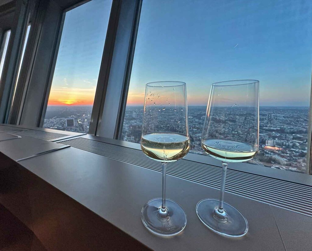 Zwei Weißweingläser auf der Fensterbank im Restaurant Sphere by Tim Raue, dahinter der Blick über Berlin im Abendlicht.