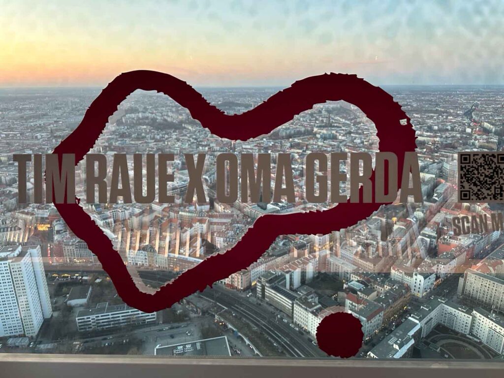 Fensterscheibe im Berliner Fernsehturm mit dem Schriftzug „Tim Raue x Oma Gerda“ und QR-Code vor dem Panorama der Hauptstadt.