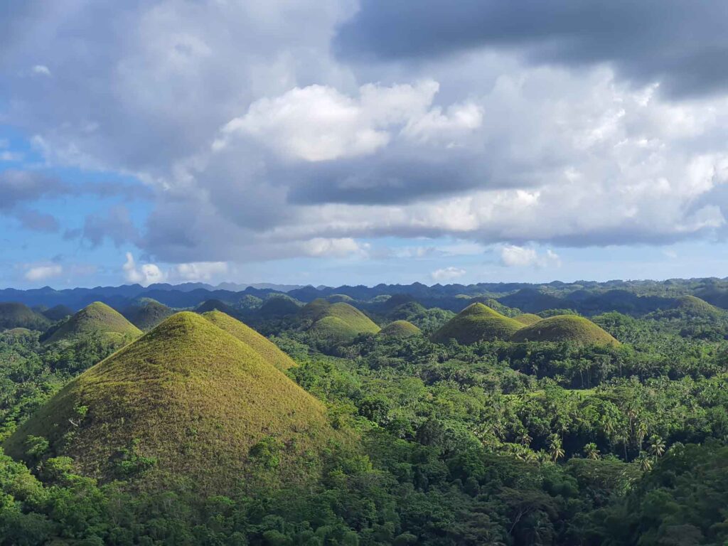 Panorama der Chocolate Hills auf Bohol mit zahlreichen kegelförmigen grünen Hügeln unter dramatischem Himmel.