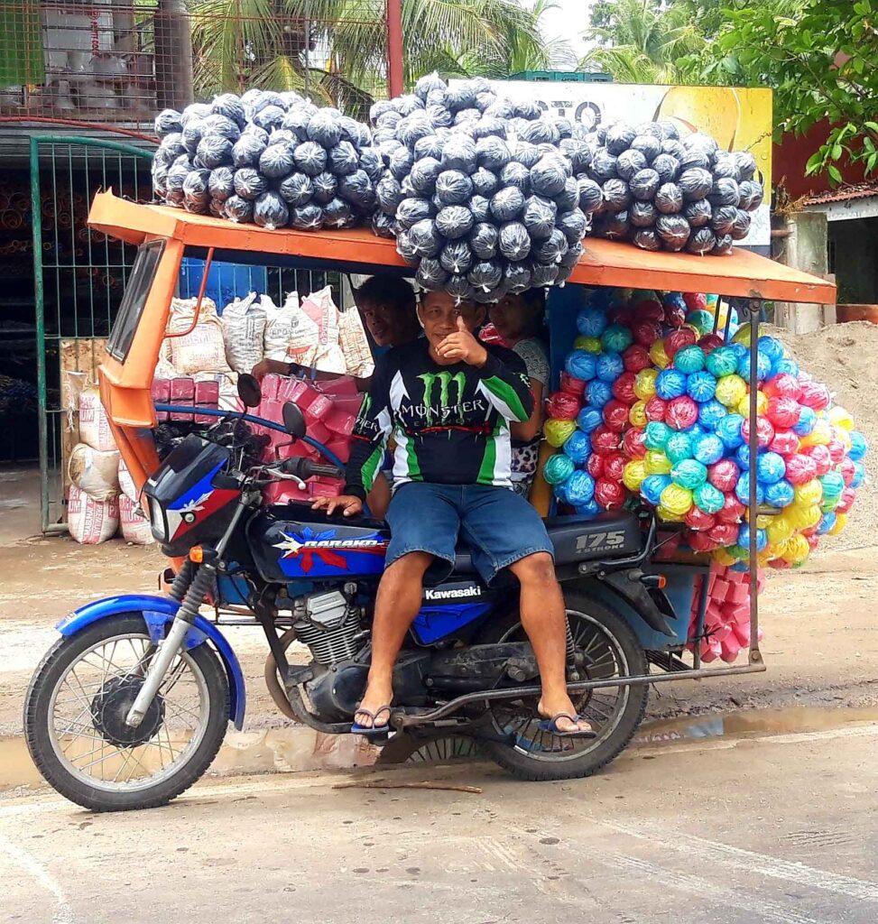 Motorrad mit Seitenwagen beladen mit vielen Plastiksäcken und bunten Verpackungen auf einer Straße auf Bohol.
