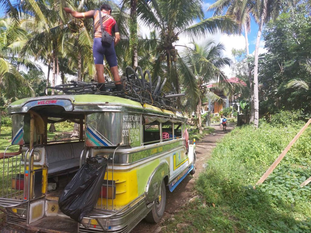 Jeepney auf ländlicher Straße mit Fahrrädern auf dem Dach und Guide, der oben steht.