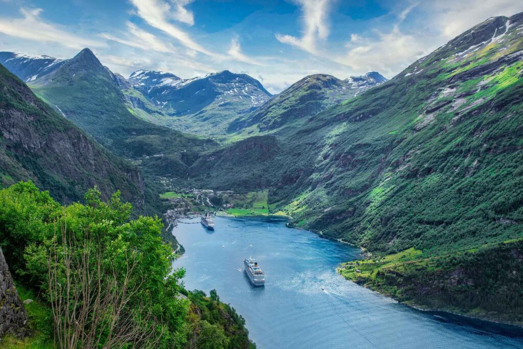 Zwei Kreuzfahrtschiffe fahren durch den Geirangerfjord, umgeben von steilen grünen Bergen und Wasserfällen in der norwegischen Fjordlandschaft.